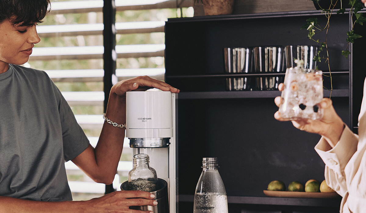 Ekspres SodaStream DUO Biały widok na osobę przygotowującą napój na tle kuchni