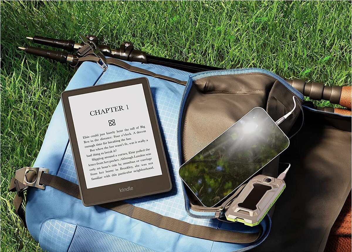 Czytnik ebook Amazon Kindle Paperwhite 5 16 GB czarny leżący na plecaku obok telefonu na trawniku