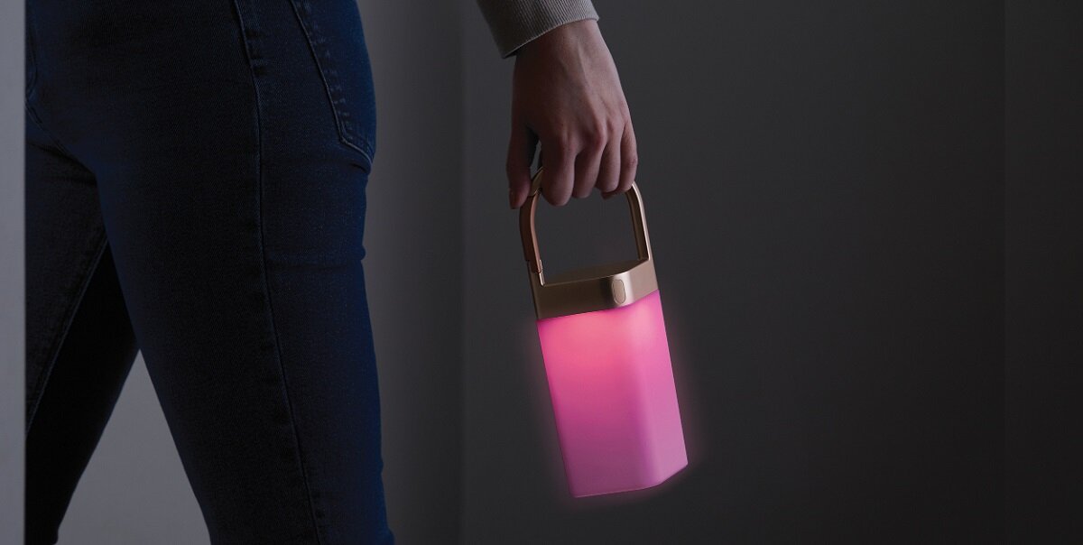 Lampa Lexon Horizon LED szara w dłoni kobiety, świecąca na różowo
