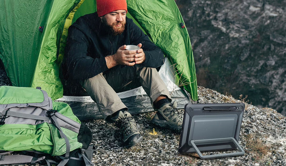 Etui Samsung Outdoor Cover do Galaxy Tab S9 grafika przedstawiająca mężczyznę oglądającego film na tablecie w deszczu w namiocie