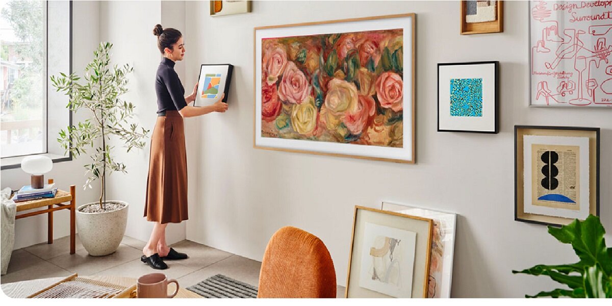 Telewizor Samsung QE65LS03DAUXXH 65” czarny grafika przedstawia kobietę wieszającą obrazek na ścianie obok telewizora w pokoju
